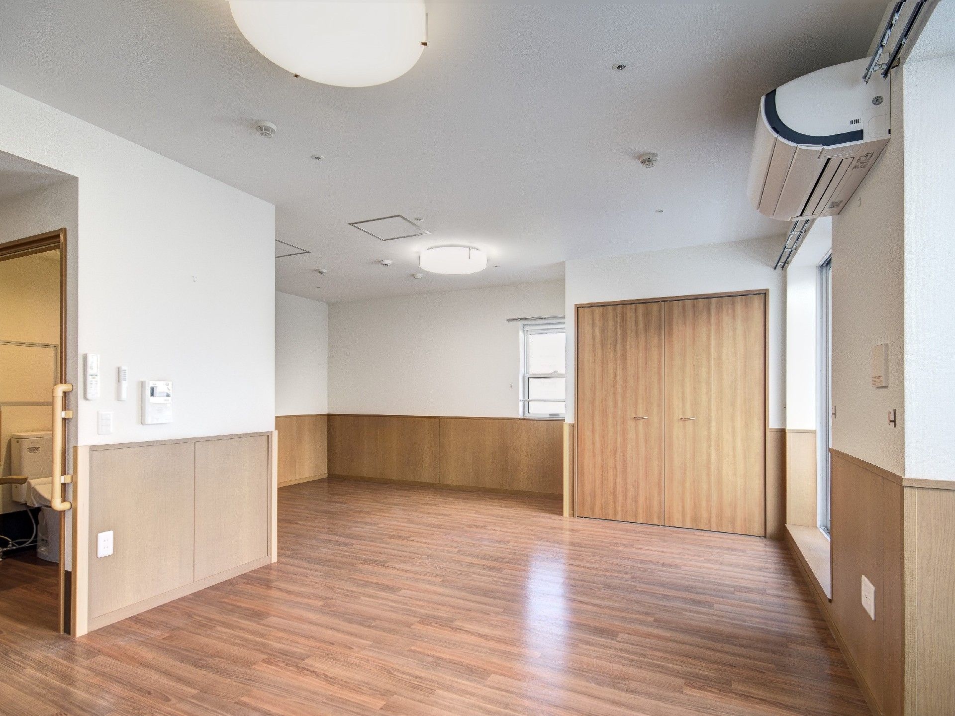 白色の壁にフローリングの部屋。床はバリアフリー構造となっている。大きな窓の隣にはエアコンが設置されている。