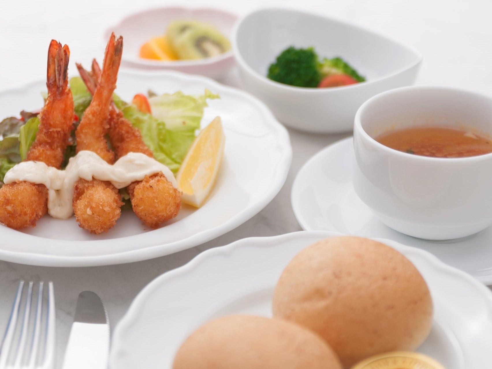 白い食器に盛りつけられた食事。メインは海老フライ、主食はパン、その他にスープ、サラダ、果物が並べられている。