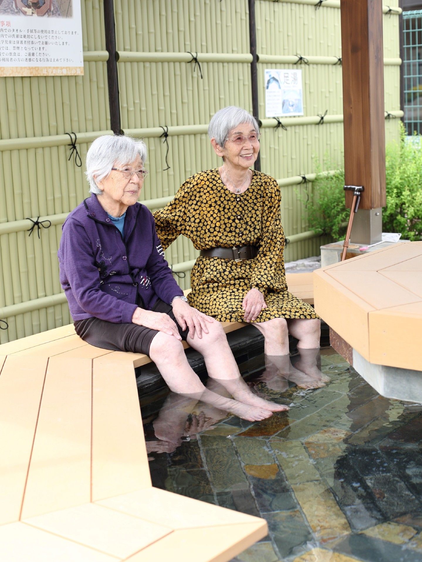 ズボンとスカートを膝上まで上げ、足湯に浸かっている入居者。