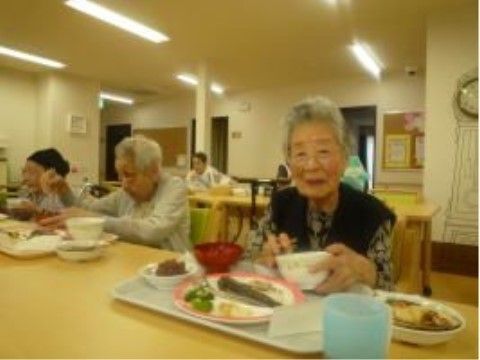 白いトレイに配膳された食事を食べながら微笑んでいる女性