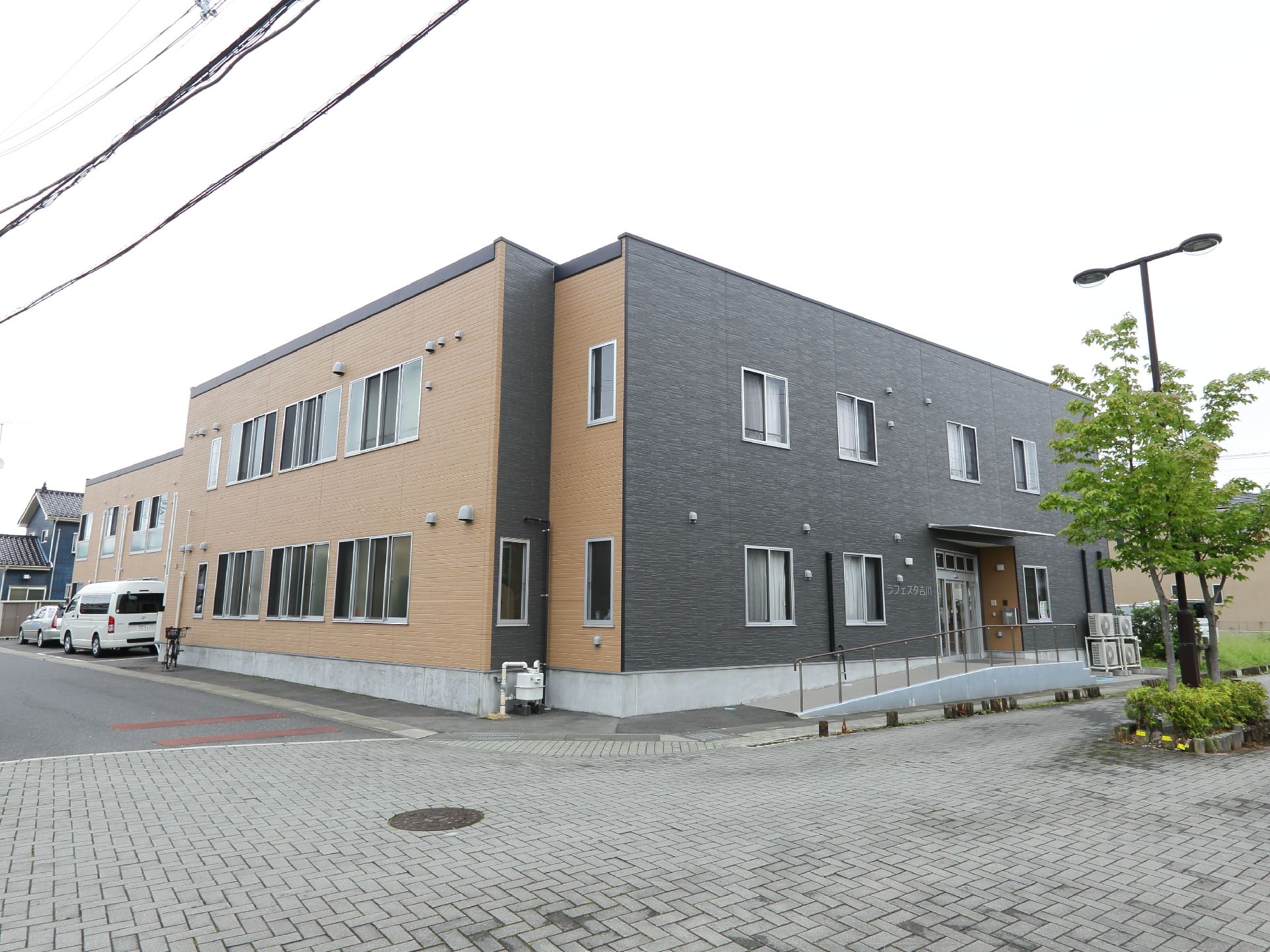高齢者向けの住宅施設はブラウンとブラックを基調とした外壁になっている。また敷地内には駐車スペースが用意されている。