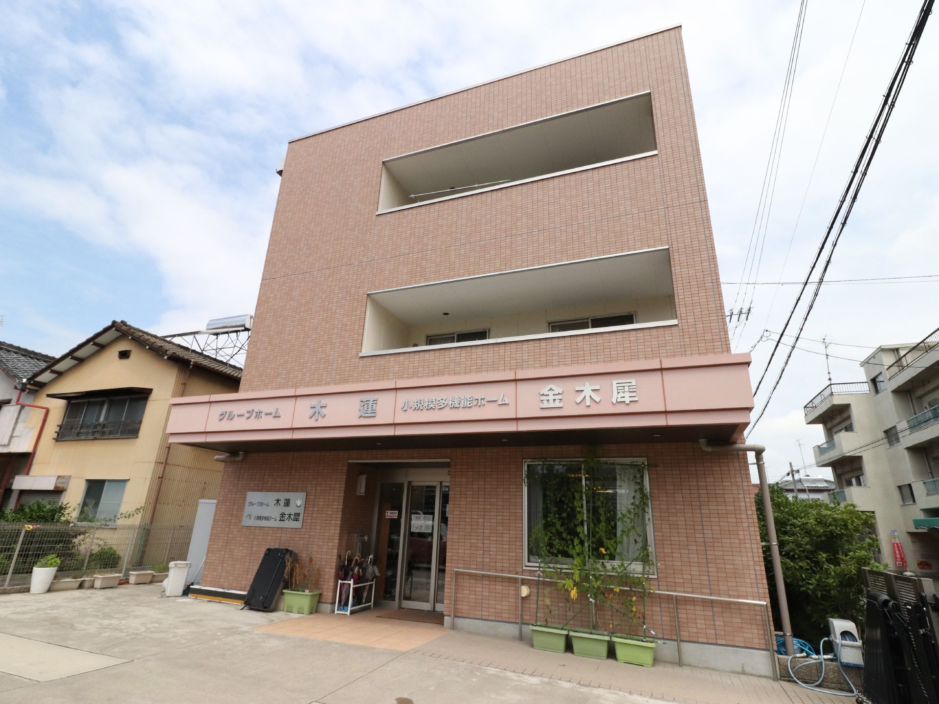 フェンスで囲まれて施設の玄関前には、プランターが置いてある。玄関前はなだらかなスロープになっていて手すりがついている。