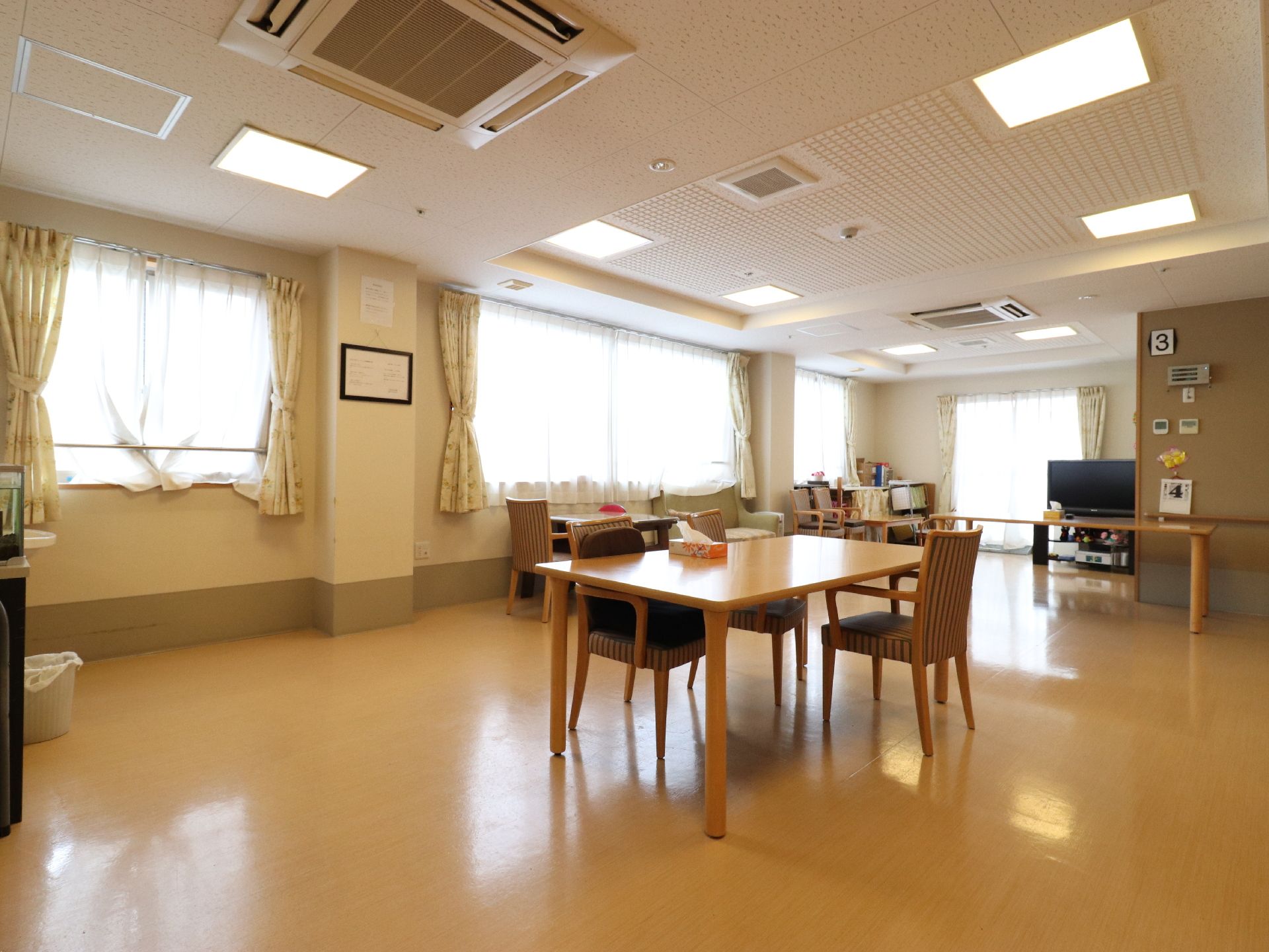 部屋には窓が四つあるのが見える。収納棚が置いてあり、一部布で目隠しがしてある。椅子が数脚置いてある。