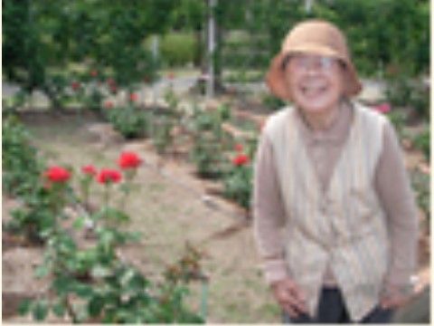 赤いバラが咲いている花壇の前で立って笑っている女性