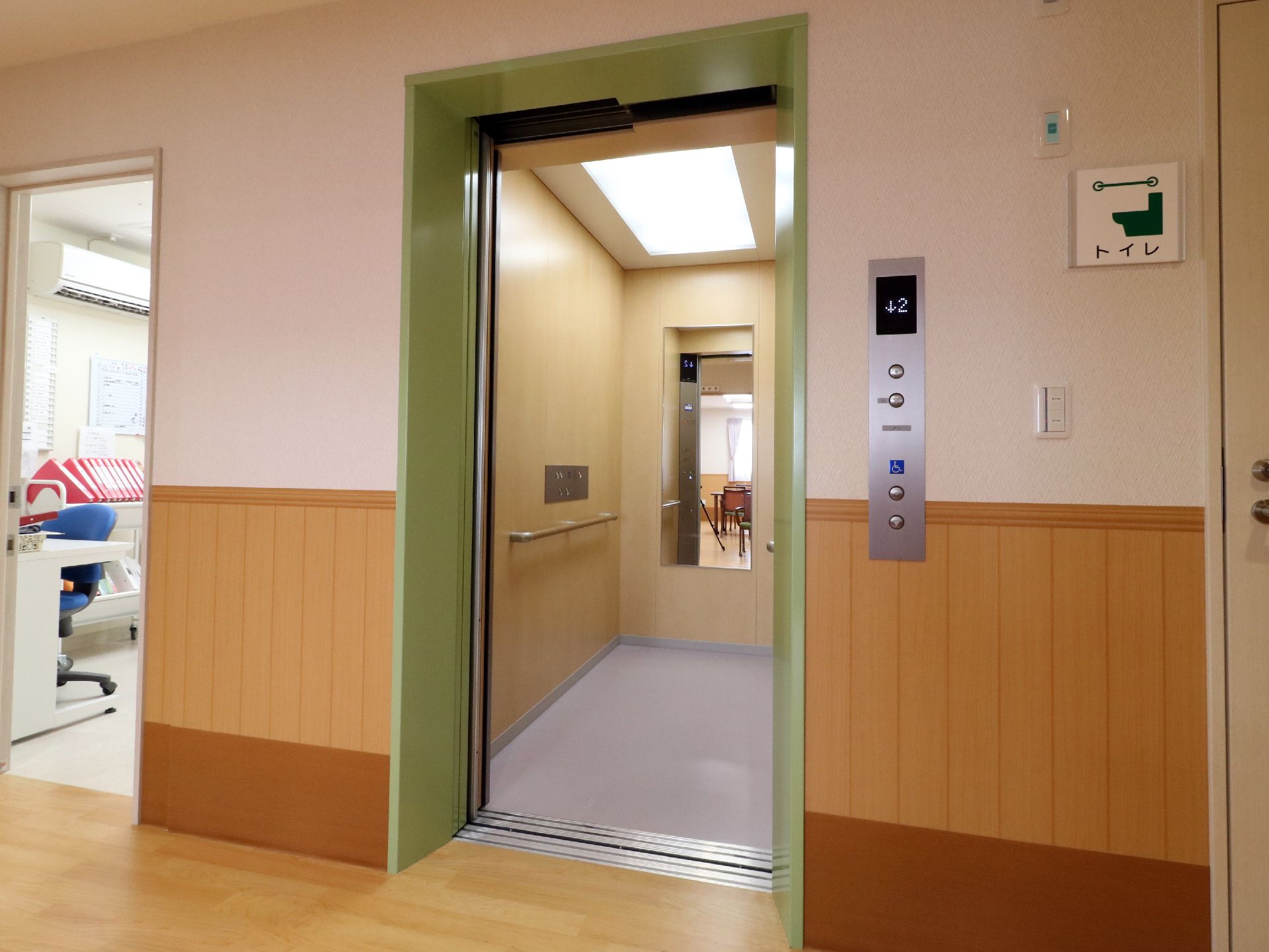緑色のドアが付いたエレベーター。内部に手すりが設置されている。