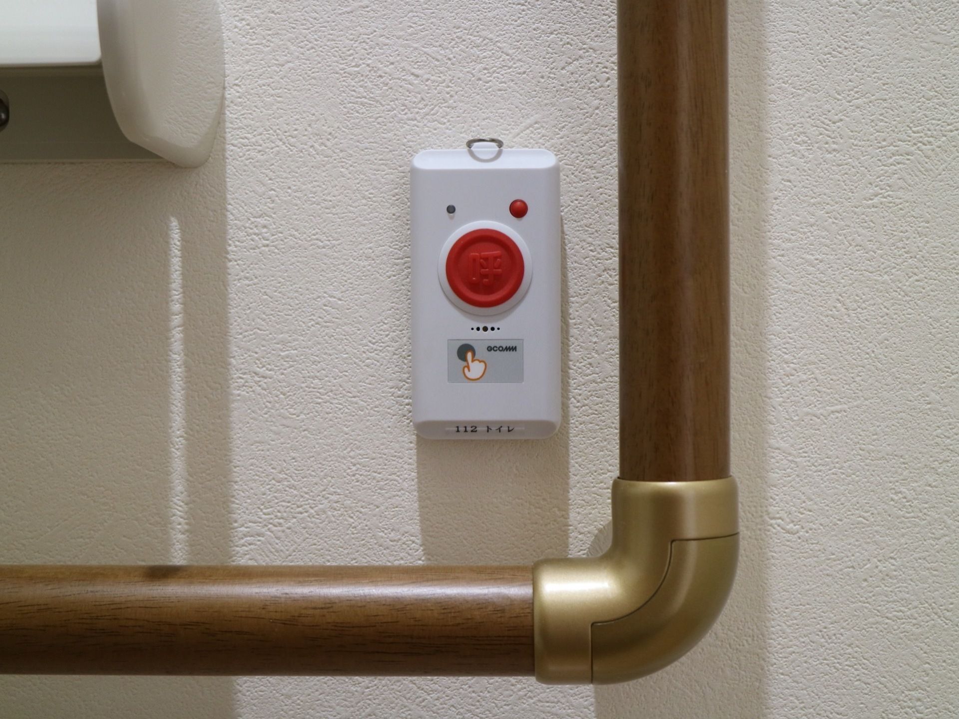 トイレットペーパーホルダーの右下に、緊急呼び出しボタンが設置されている。ボタンの横に手すりが設置されている。