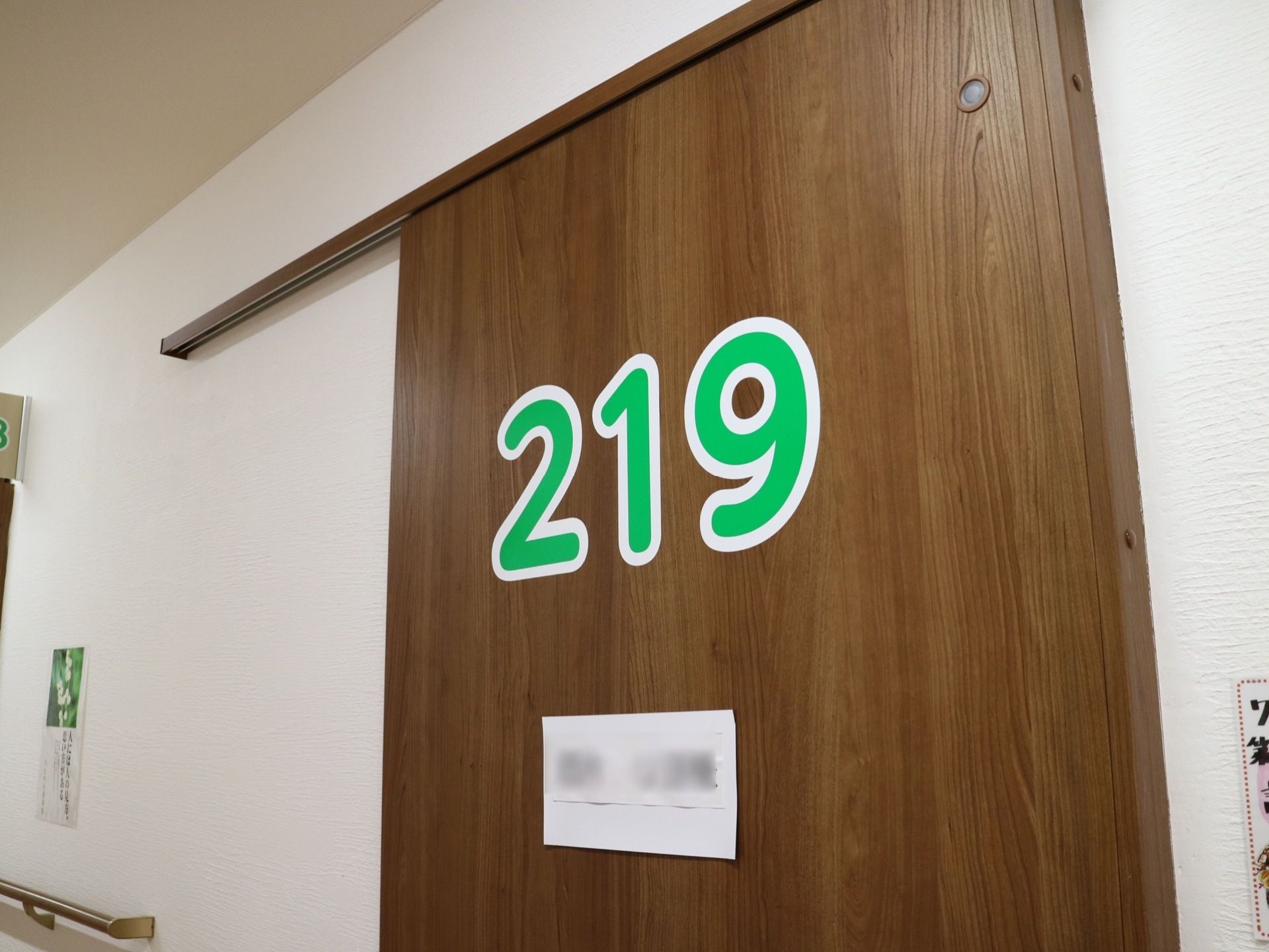 居室のドアはダークブラウンの木目調で、スライド式である。部屋番号がドアの中心部分に緑の文字で大きく表示されている。