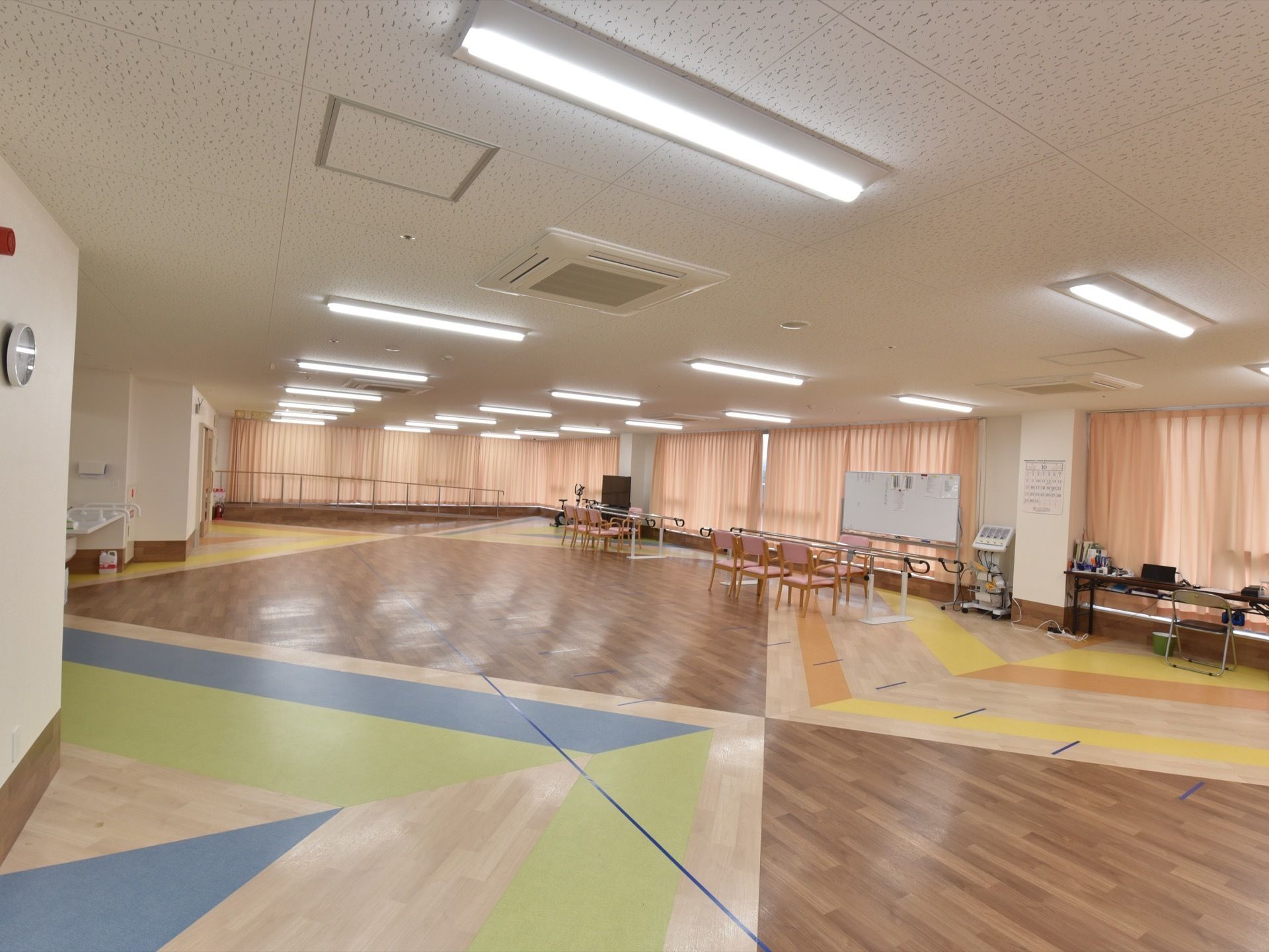 機能訓練室の床は、フローリングにカラフルな色が施されている。天井埋め込み式エアコンとカーテンで、空調と日照を調節できる。