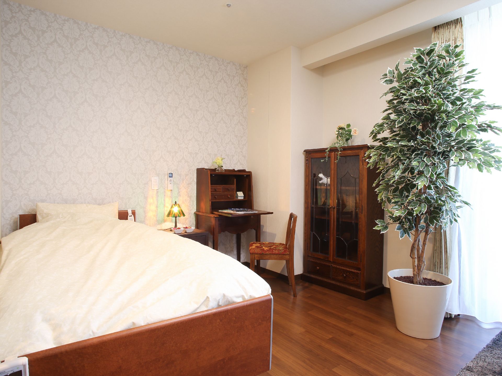 上品なデザインの壁紙が目を引く居室である。広々したベッドやテーブルセット、収納家具などが完備されている。