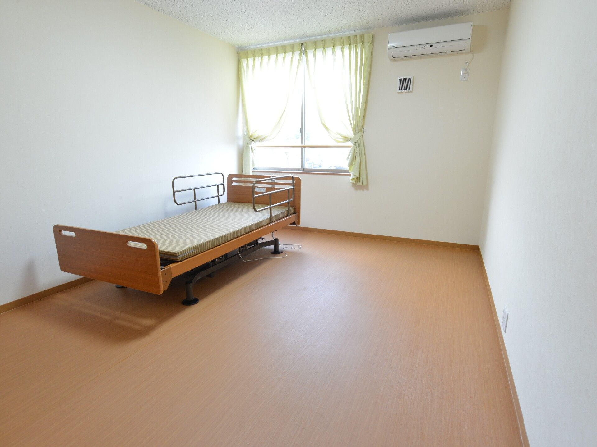 木製の介護用ベッドが窓の前に置かれている入居前の綺麗な部屋