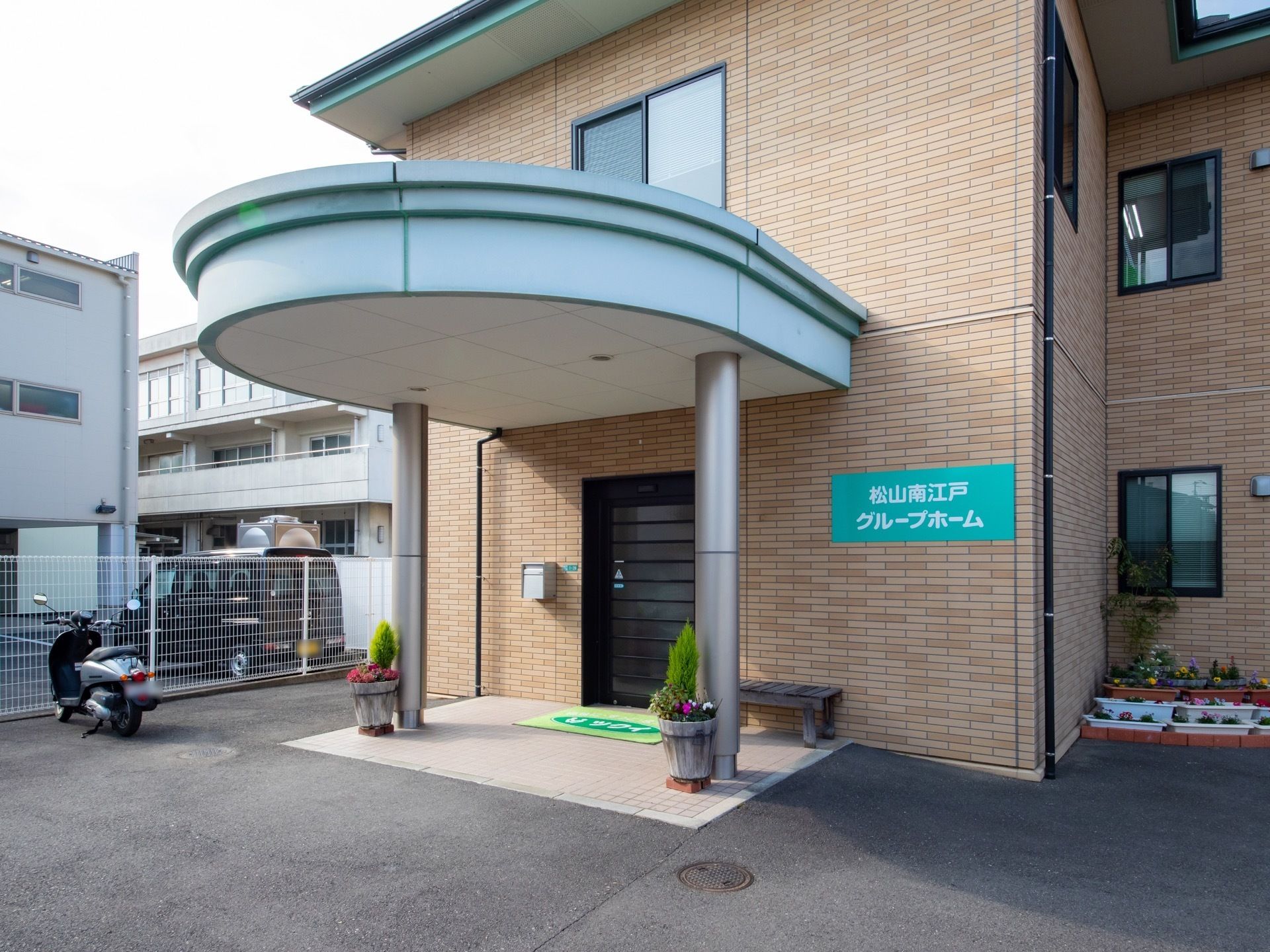 丸いエントランスの屋根がおしゃれなレンガ造りの建物である。扉は間口の広い自動ドアである。ベンチや花が植えられたプランターが置かれている。
