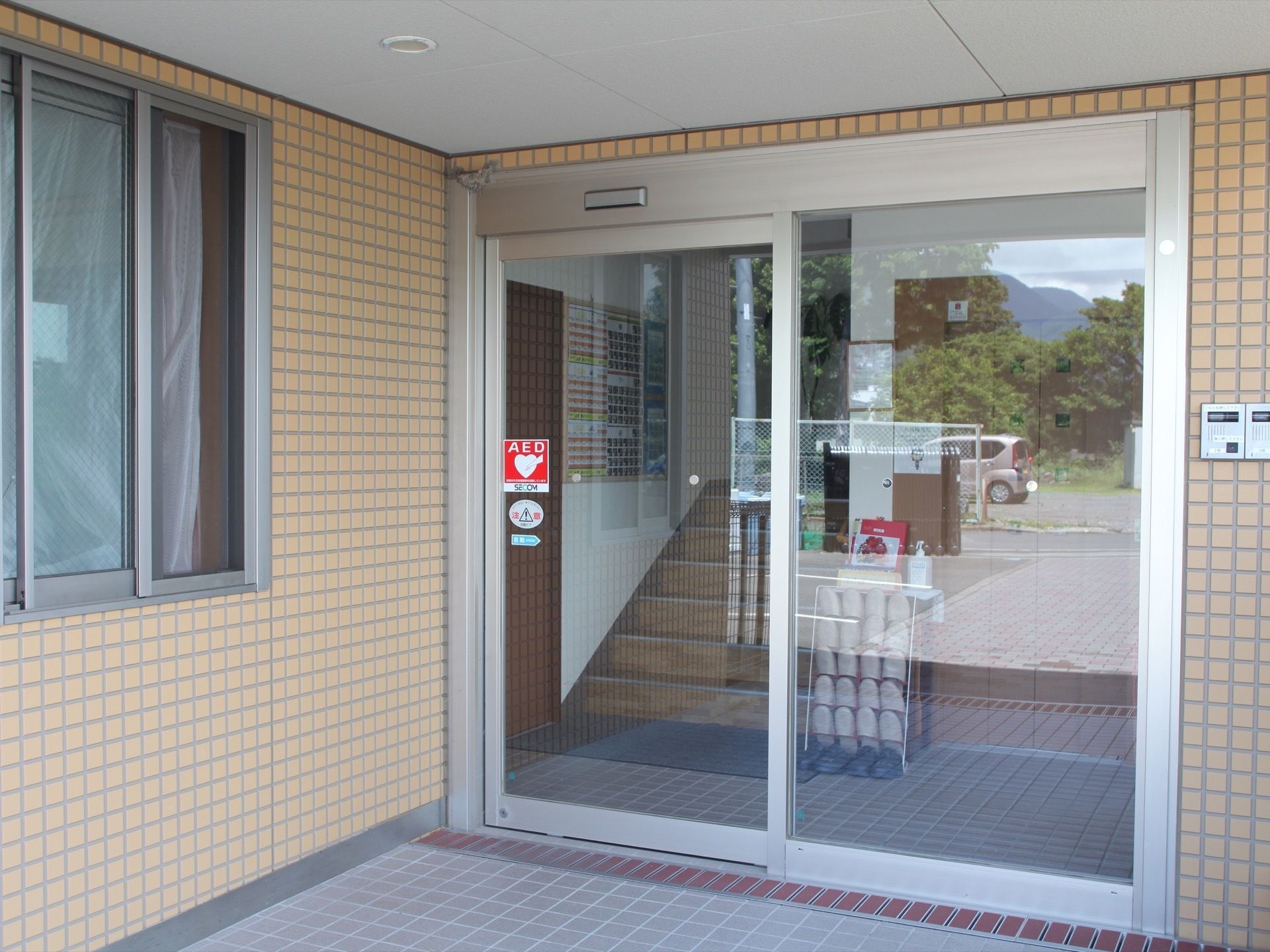 玄関の自動ドアには、AEDのステッカーが貼ってある。床は段差がなく、グレーのタイル張りになっている。