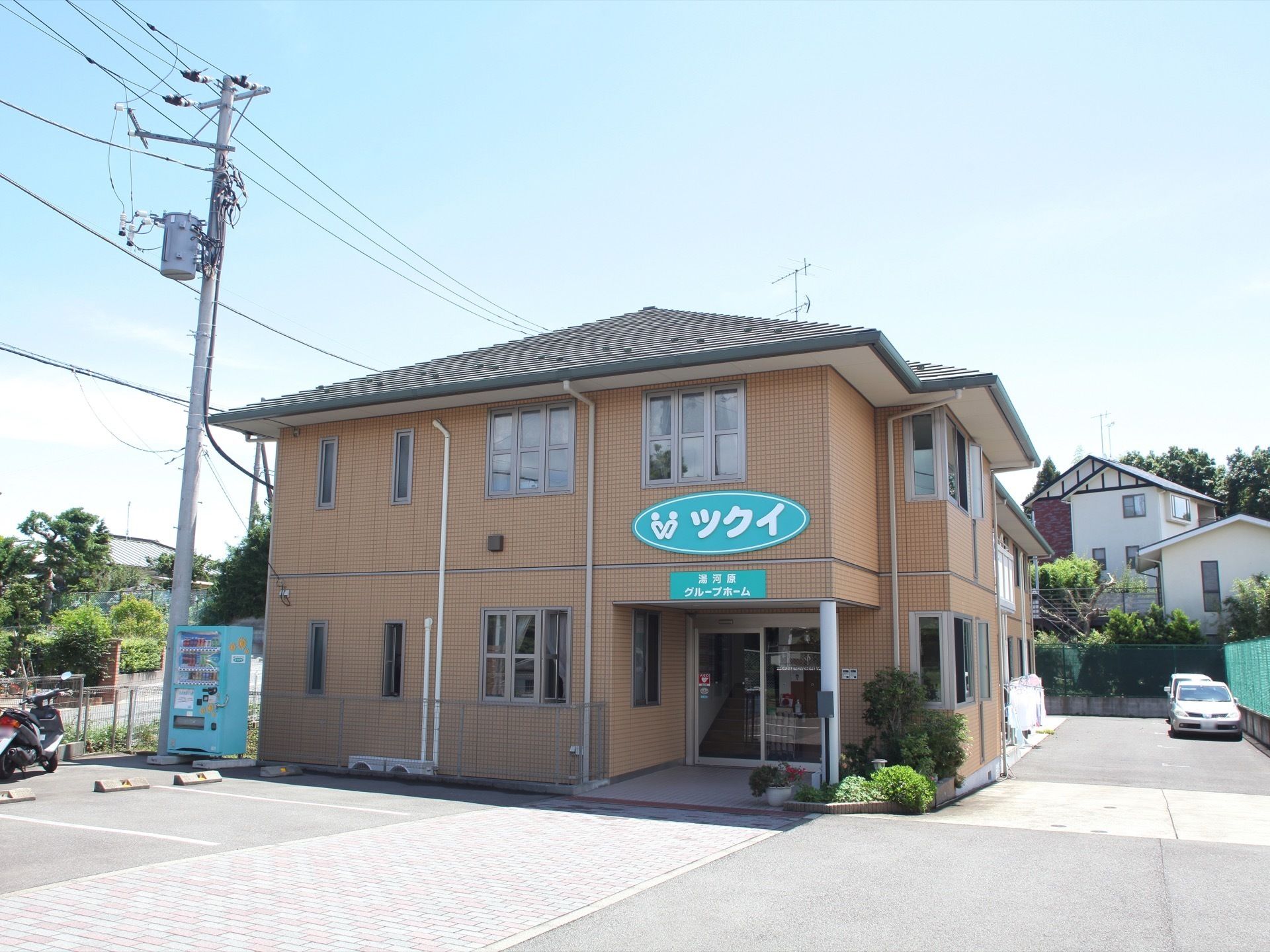 ベージュの外壁に施設名の看板が掲げられた、２階建ての建物である。建物の前や奥には駐車場があり、バイクを停められるスペースもある。