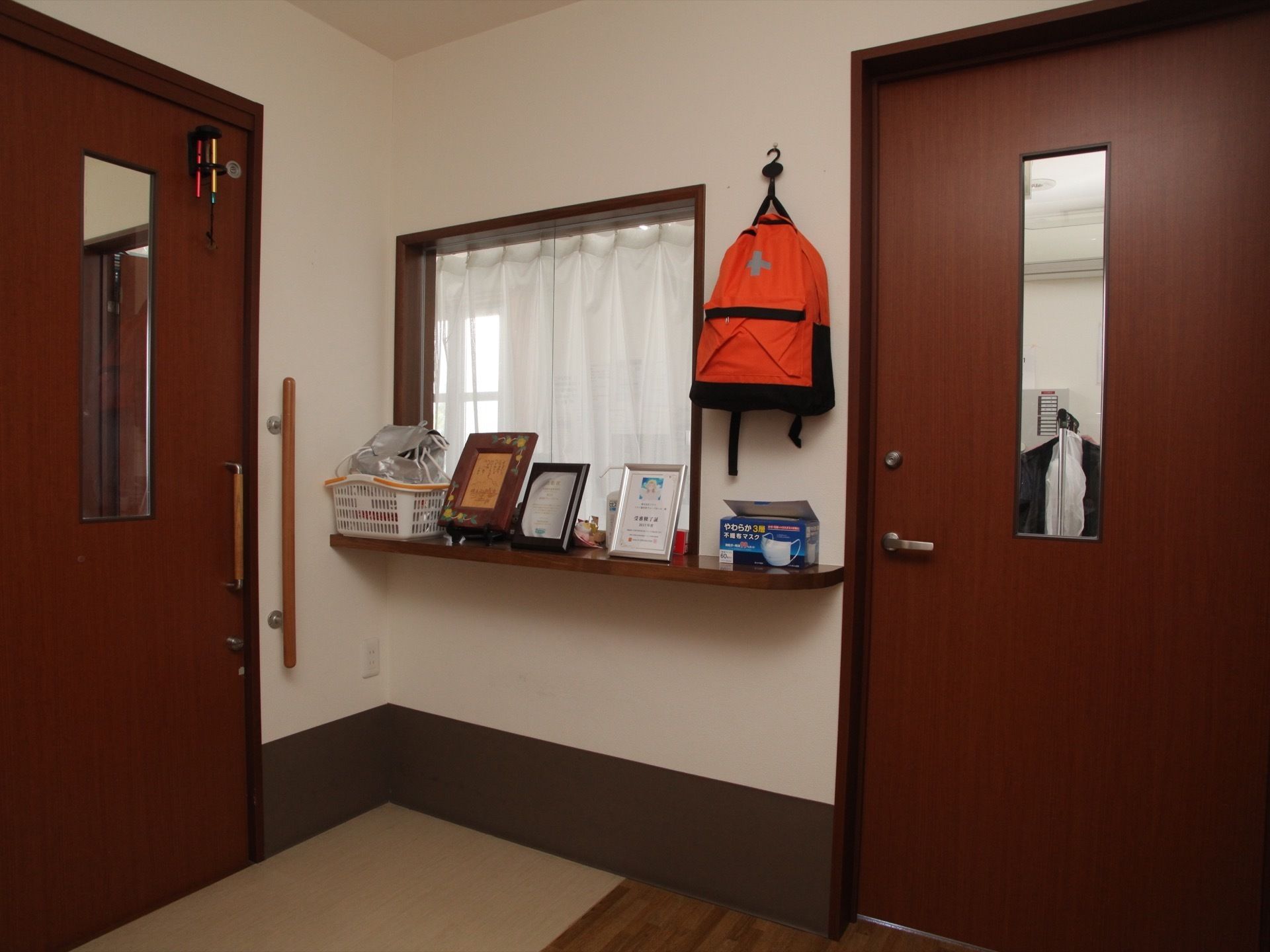 スタッフルームの窓にはレースのカーテンが掛けられ、前のカウンターにはマスクや額、写真立てのようなものが置かれている。