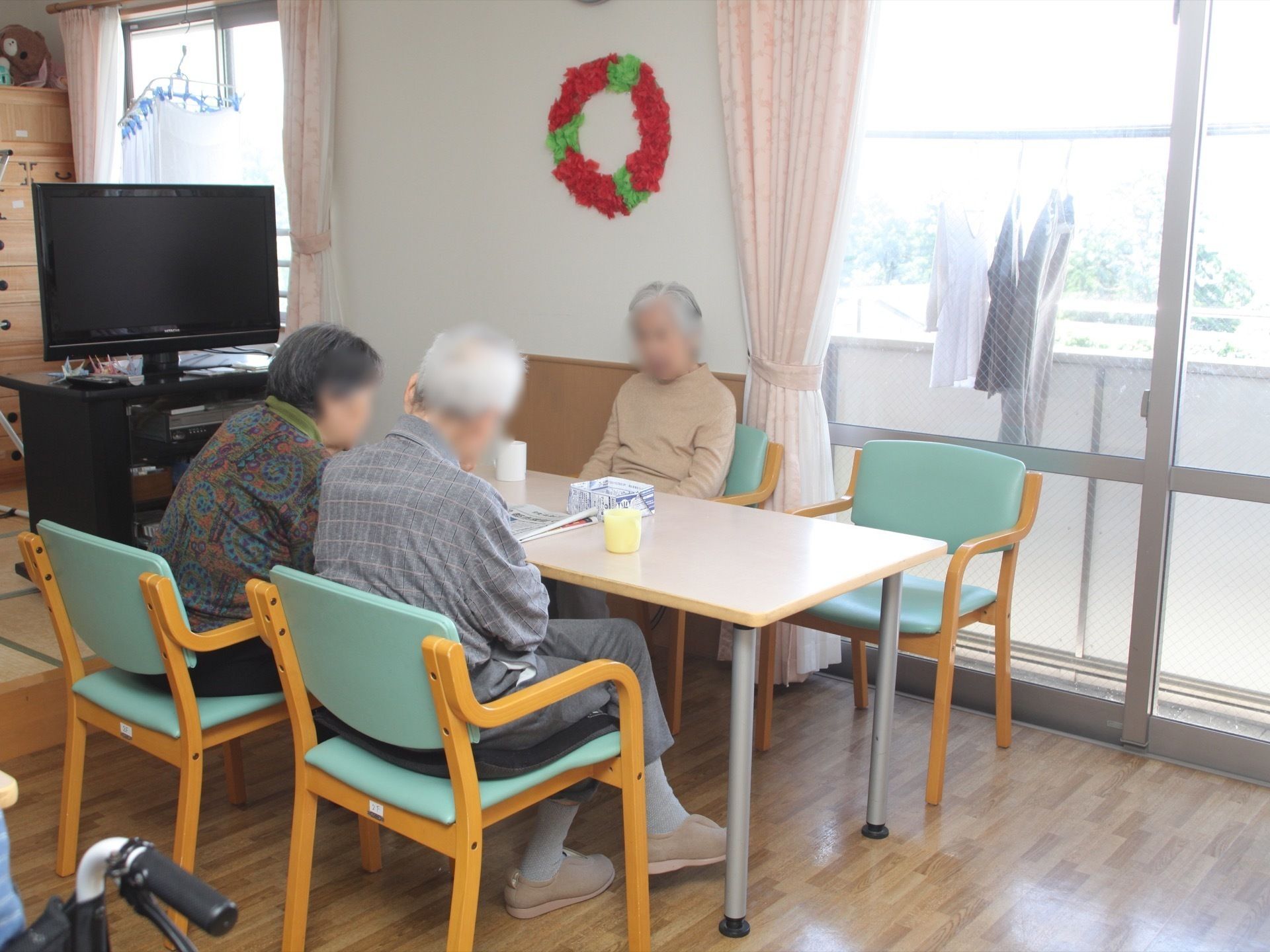 緑の椅子が置かれたテーブルセットに集まって会話を楽しむ入居者様