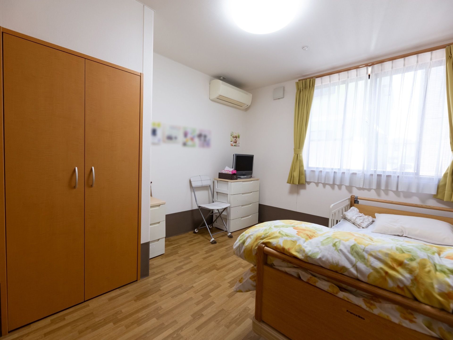 フローリングの部屋には備えつけのクローゼットがある。壁にはエアコンがついている。壁際にはベッドが置かれている。