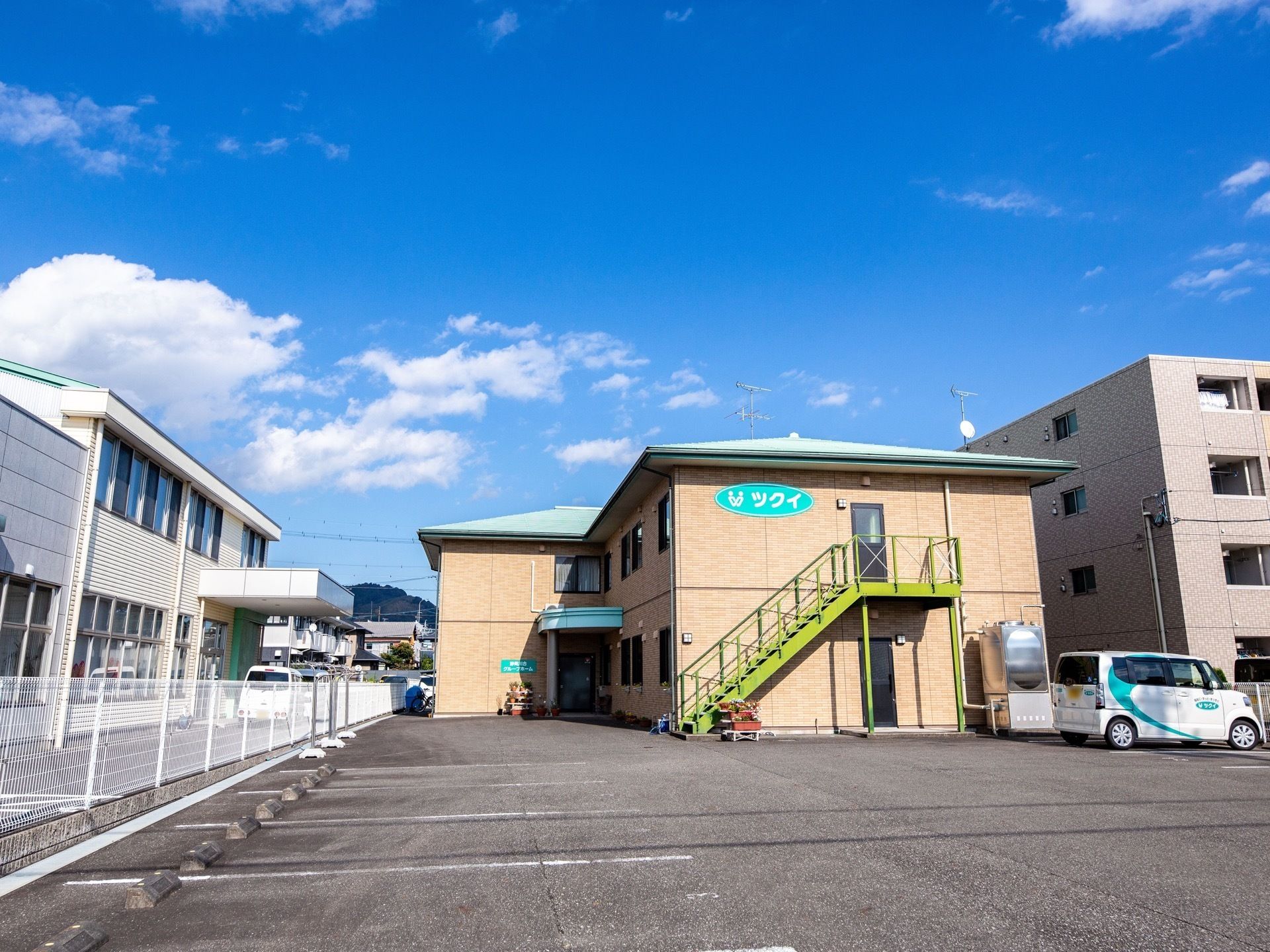 ホームの建物の前には広い駐車スペースが広がっている。ホームの送迎車が一台、建物のすぐ横に停まっている。