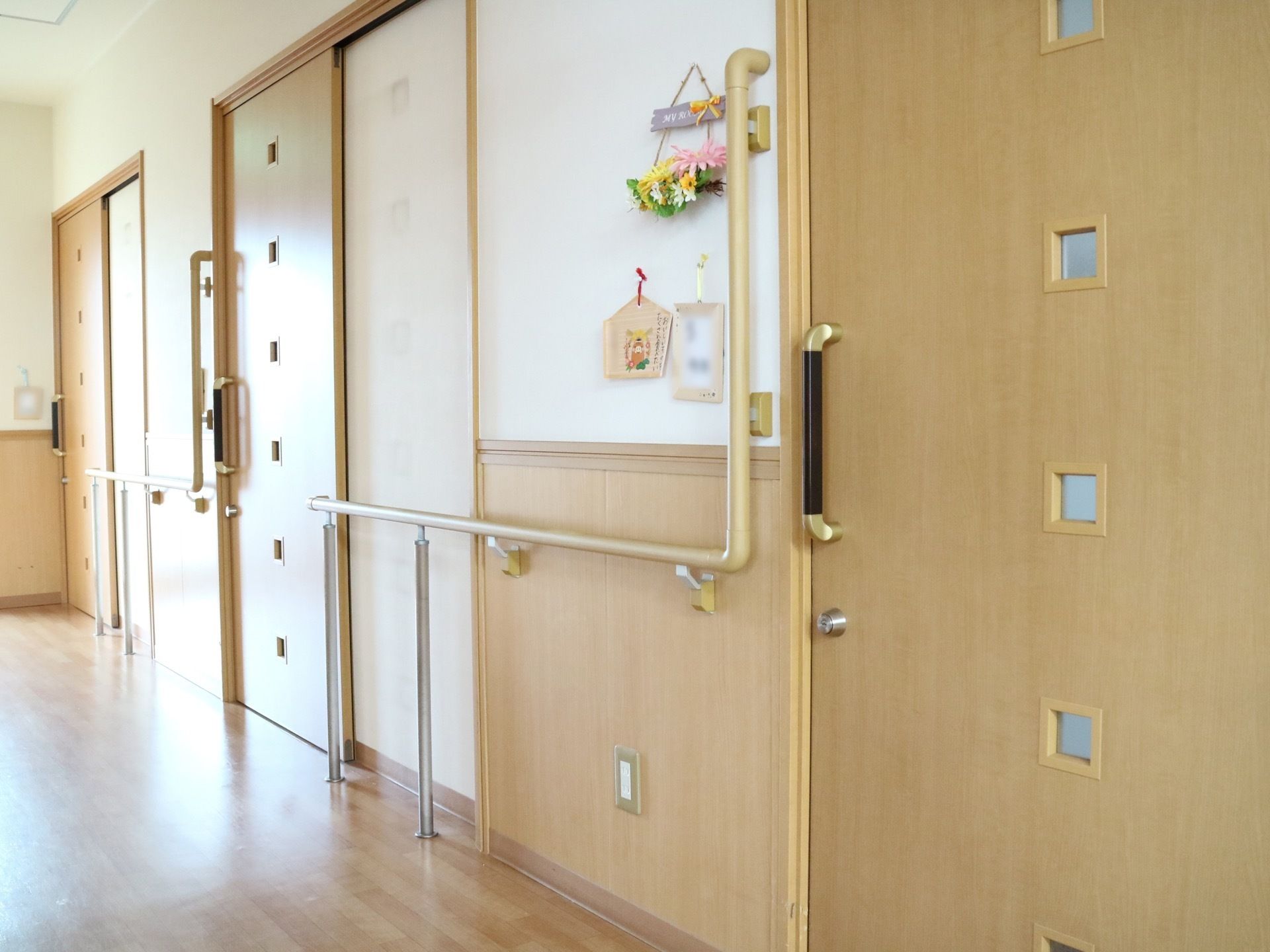 フローリングの床の廊下が左奥に向かって伸びている。３ケ所に引き戸があり、四角い窓が６つずつ開いている。