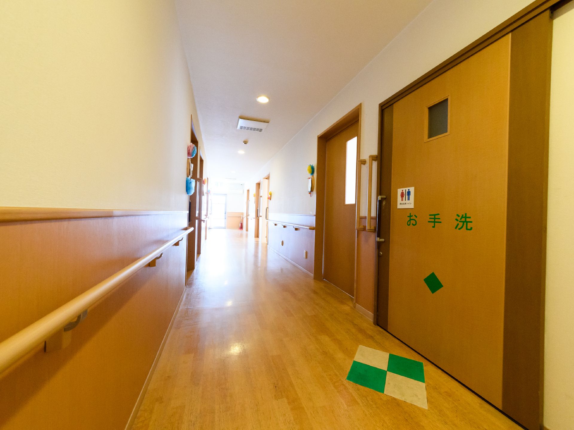 廊下の奥には窓があり、陽が差し込んでいる。入居者が共同で使用するトイレのドアには大きな字で「お手洗」と書かれ、床にも分かりやすくマークが付いている。