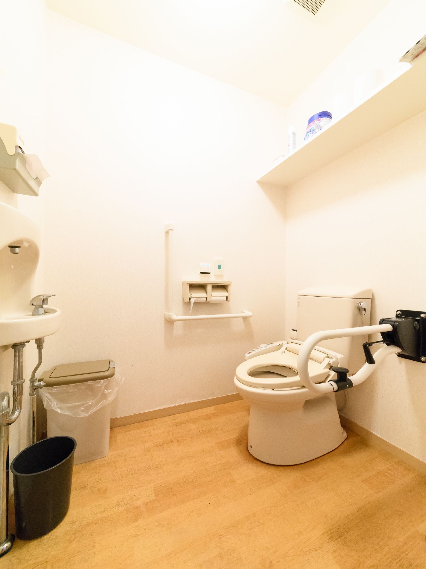 トイレ空間は広く、洋式トイレと手洗い場が設置されている。上部の壁には棚もある。手すりやナースコールが備えられている。