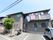 2階建ての施設の手前には、道路に面した3台分の駐車スペースがある。向かって左側の植木の所が出入り口になり、階段やスロープがある。