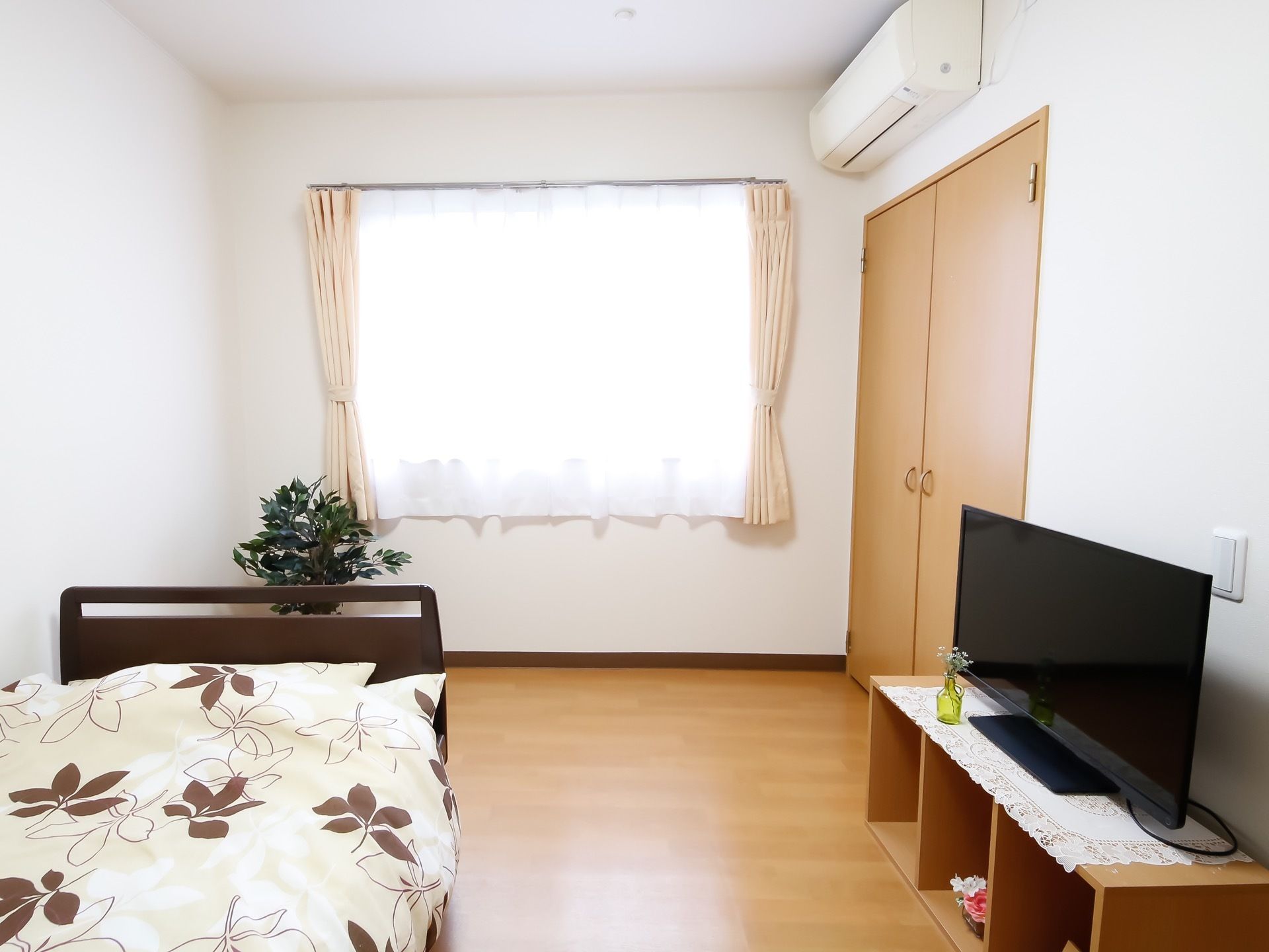 明るい光が差す大きい窓に清潔感を感じる白いカーテンが設置されている。大きいＴＶに収納スペースも完備している。