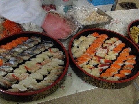 大きな丸い桶にたくさん並べられたお寿司と、準備をするスタッフ