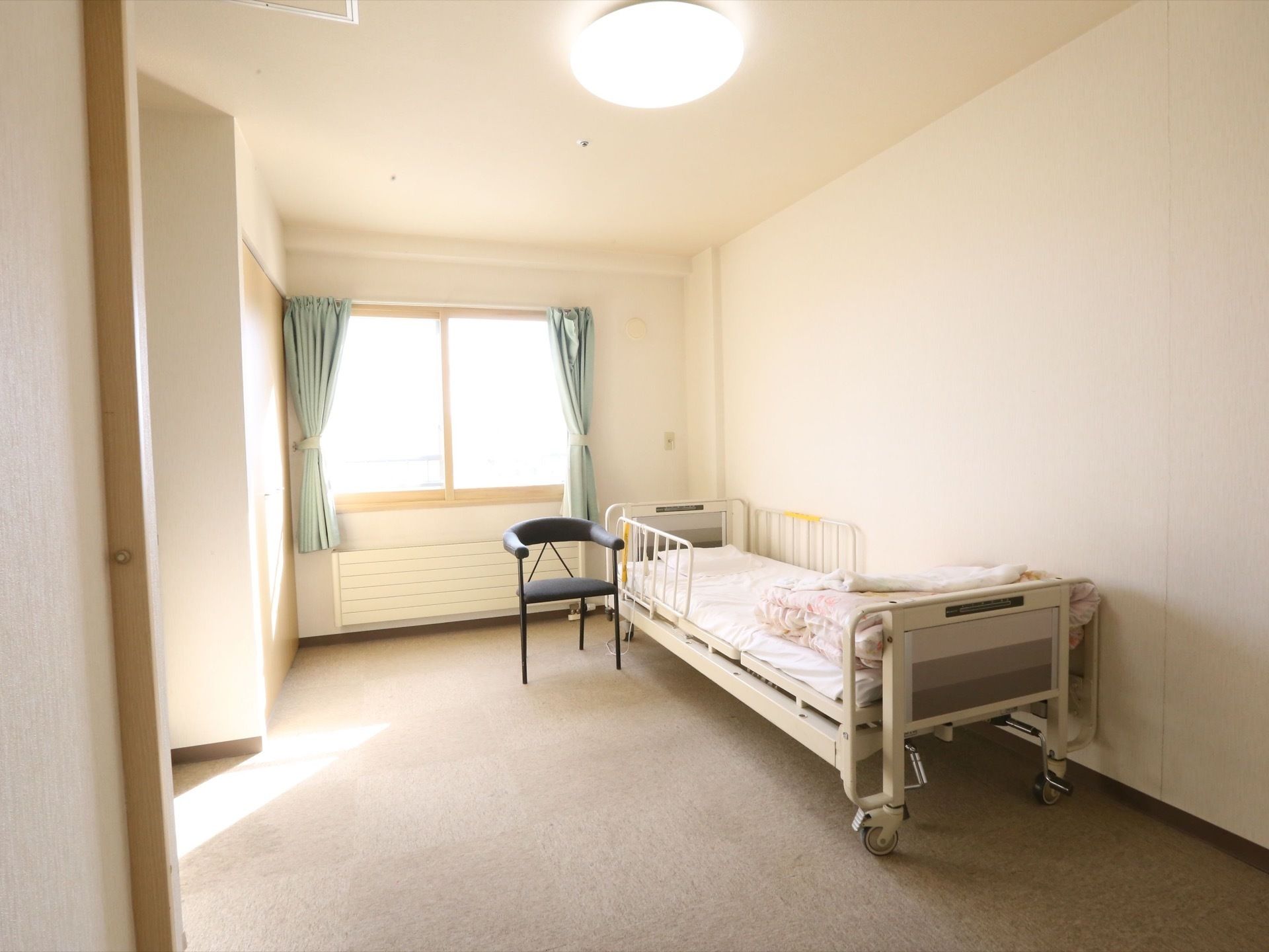 白を基調とした居室で、とても日当たりが良い。キャスター付きのベッドや椅子、暖房器具が完備されている。
