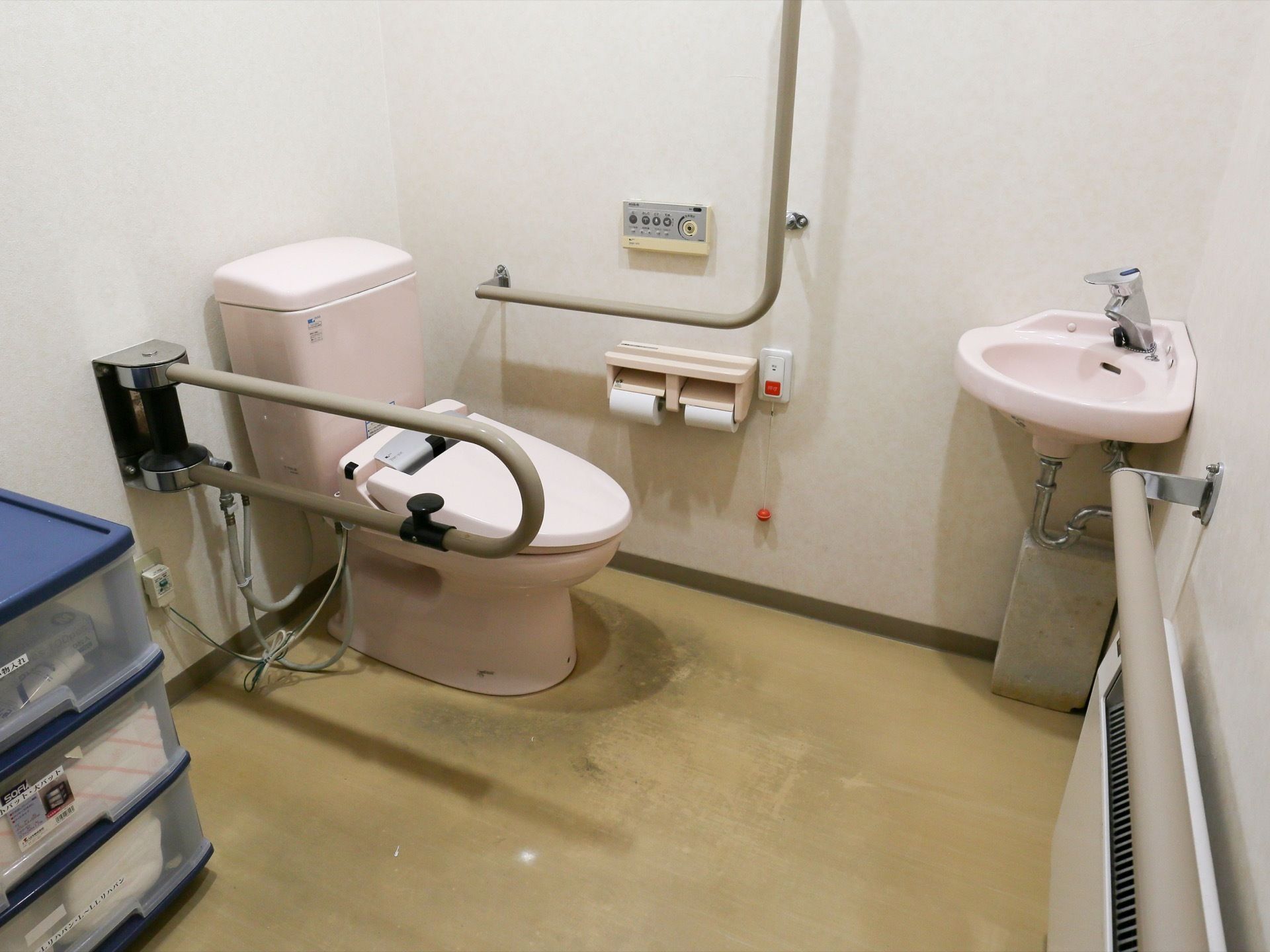トイレには簡易手洗い場があり、広々とした空間となっている。壁際には、青い収納ボックスが置かれている。