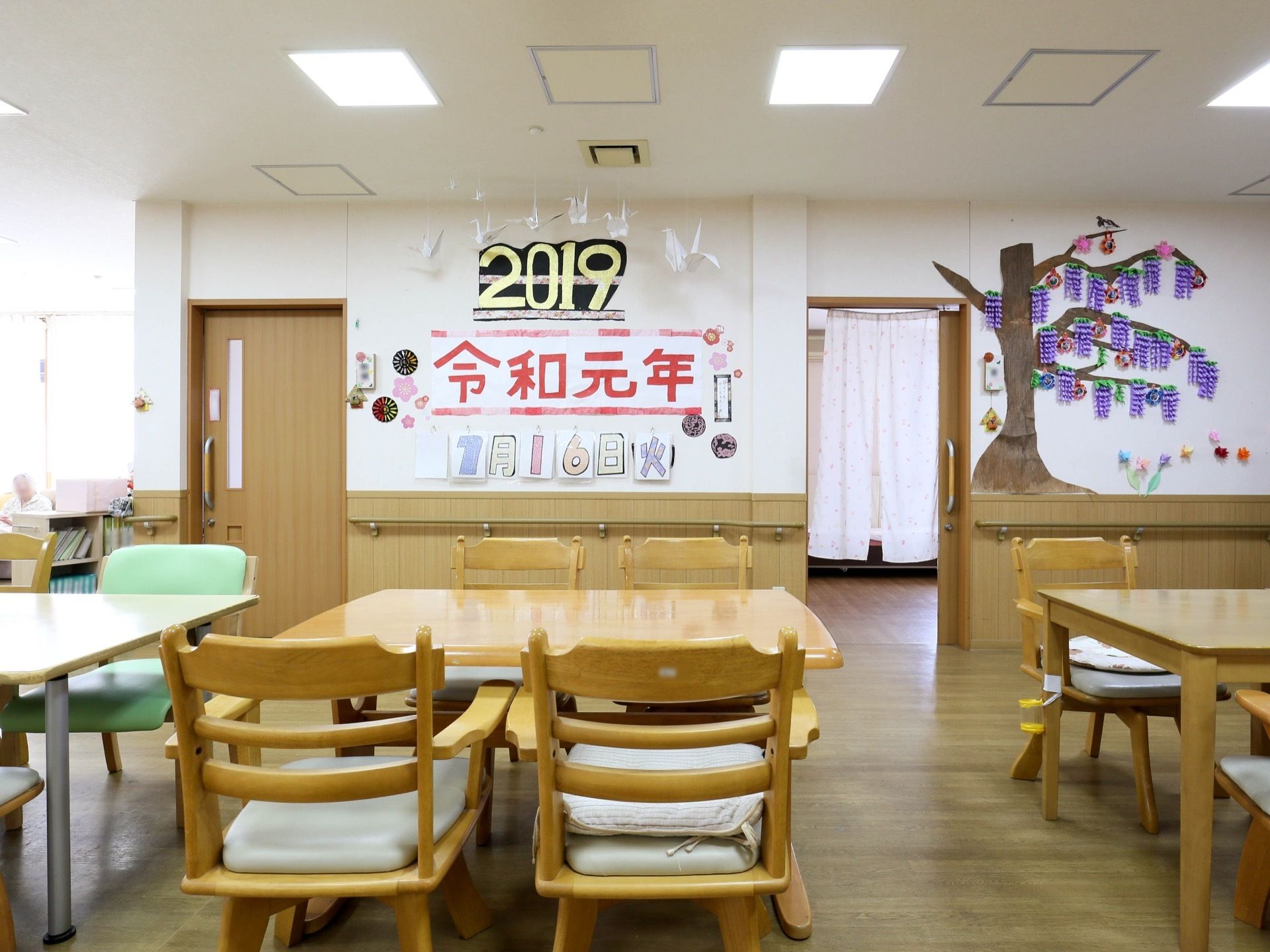 施設内には共有スペースがあり、壁には大きく日付が書かれている。中央には、たくさんの4人掛けテーブルが並べられている。
