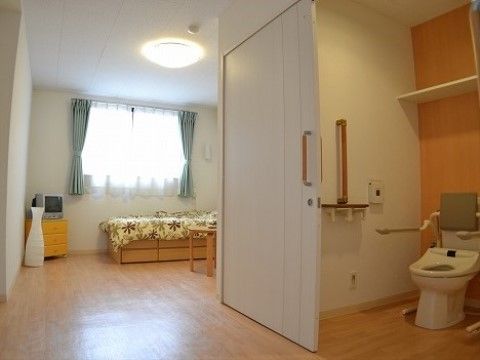 テレビとベッドがあり、手前のトイレには手摺があり床は段差のない居住空間