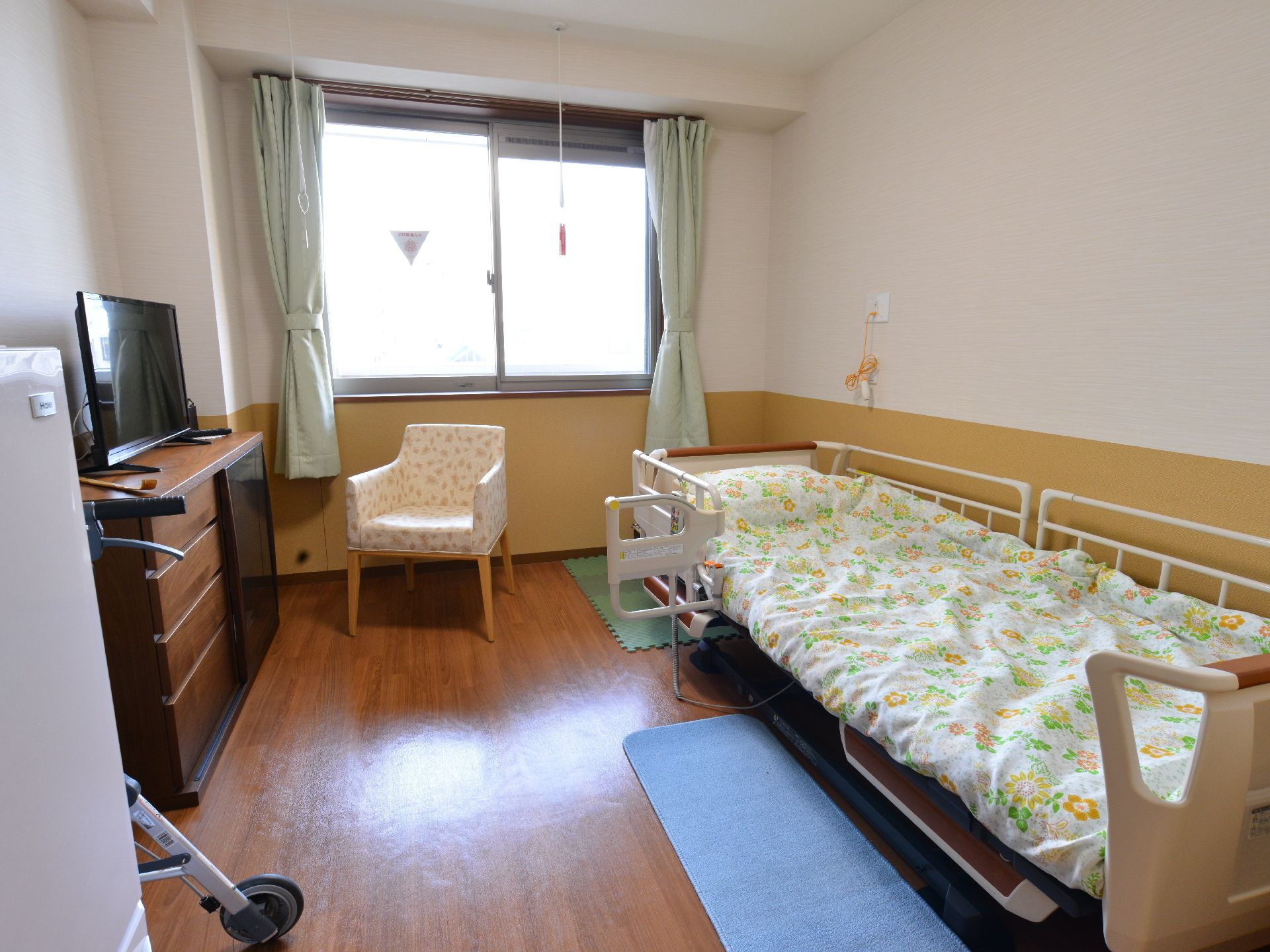 花柄の布団が敷かれた介護用ベッドが用意されている居室