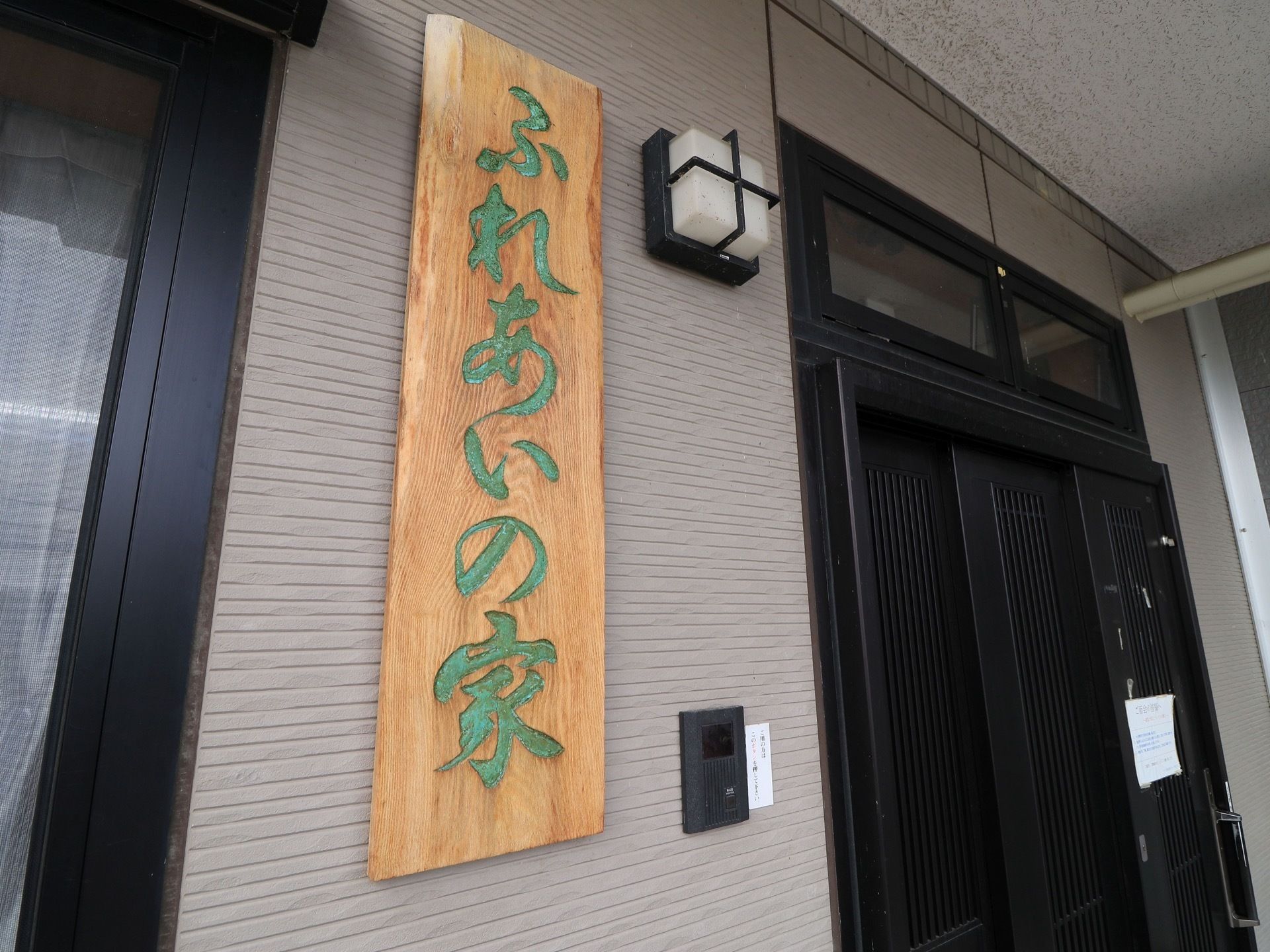 木材で作られた看板がドアの横に掛けられている。横開きの間口の広いドアが採用されている。頭上に屋根がついている。