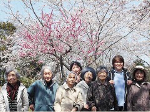 白やピンクの梅の花が咲いている木の下で笑っている入居者様