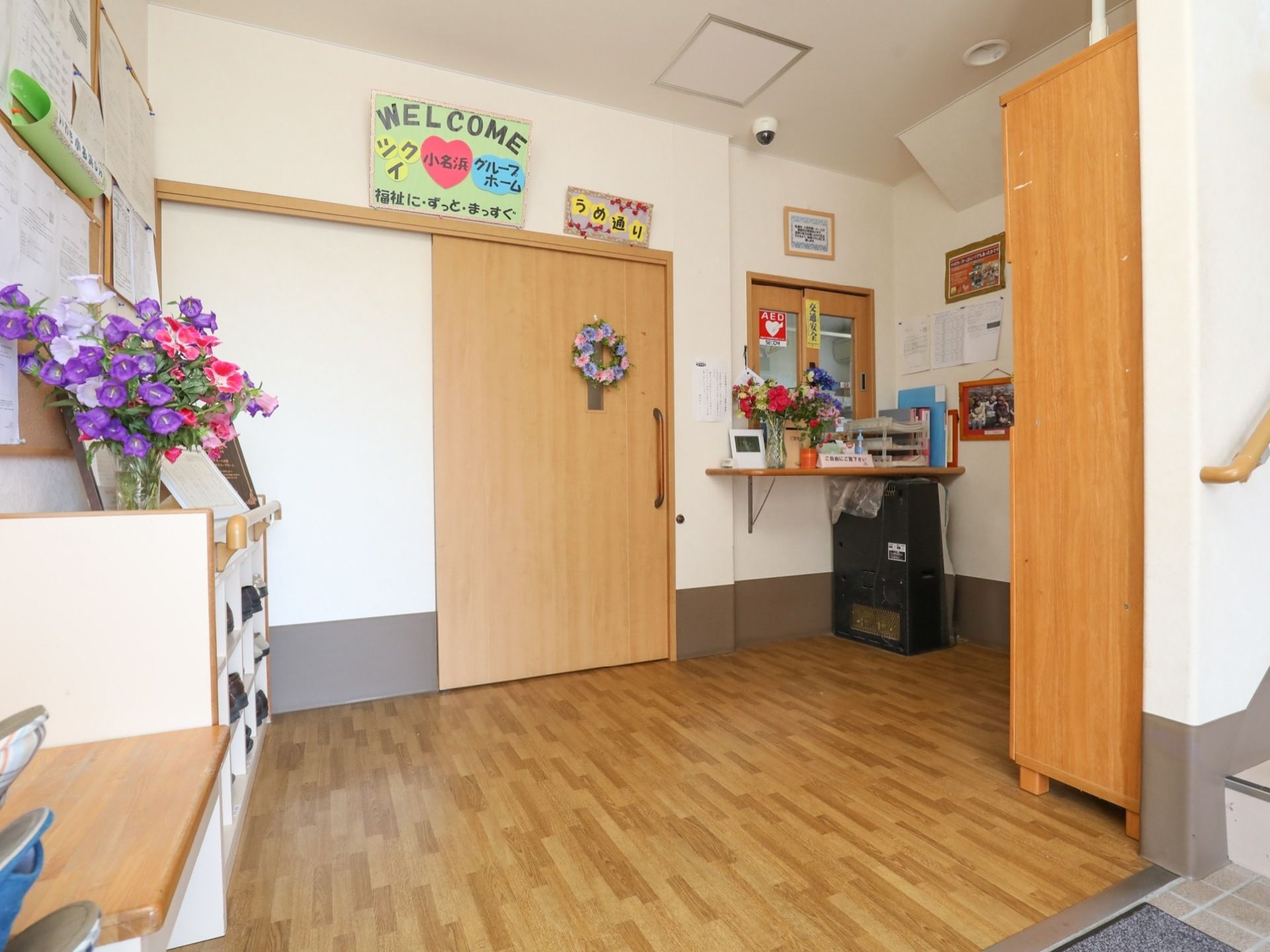 玄関は木の質感を活かしたナチュラルな雰囲気である。受付の窓口があり、花や手作りの装飾が飾られている。