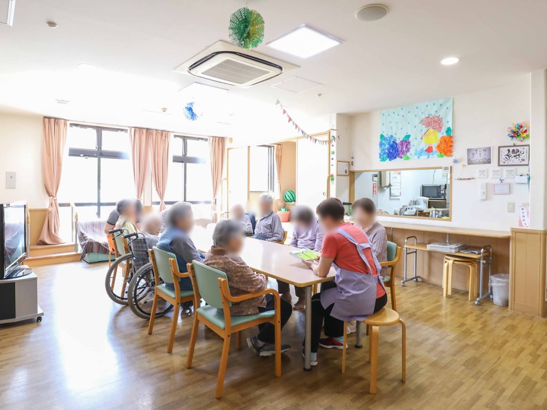 入居者様が大きな窓から明るい日差しの入る空間で、レクリエーションを楽しんでいる。大型のエアコンが設置されている。