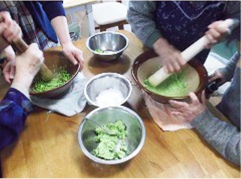 大きなすりこぎ棒で緑色のだんごをこねている入居者様