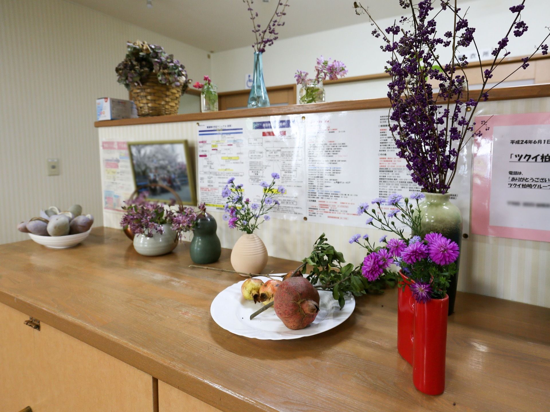 木製の棚の上に飾られたオブジェなどの図である。花瓶に生けられた花や、白い皿に乗せられた木の実などが飾られている。