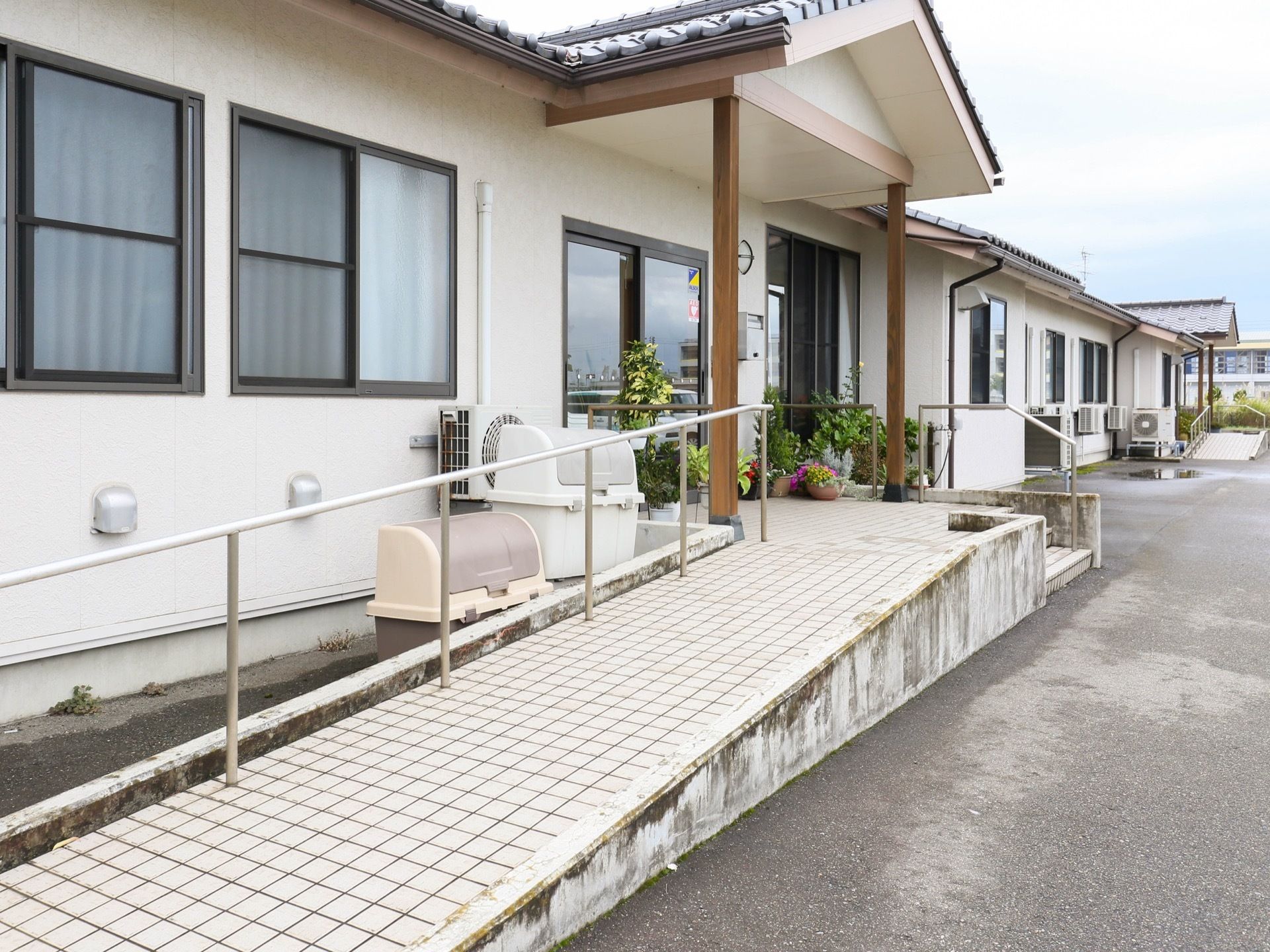 左側には施設の建物があり、奧に向かって真っ直ぐ伸びている。玄関に向かってスロープがあり、手すりがある。
