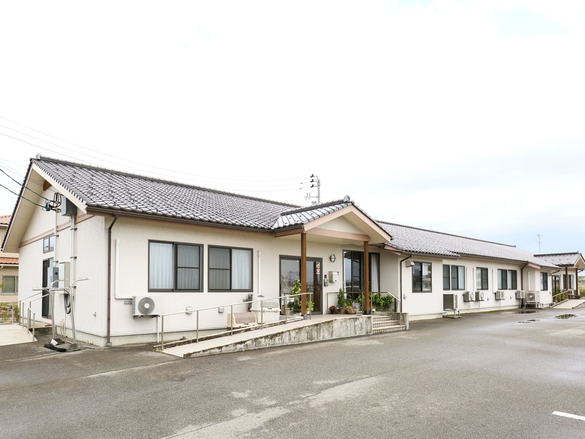 白い外壁にグレーの瓦屋根の建物で、１階だけの平屋建てになっている。窓が等間隔に並び、中央に玄関がある。