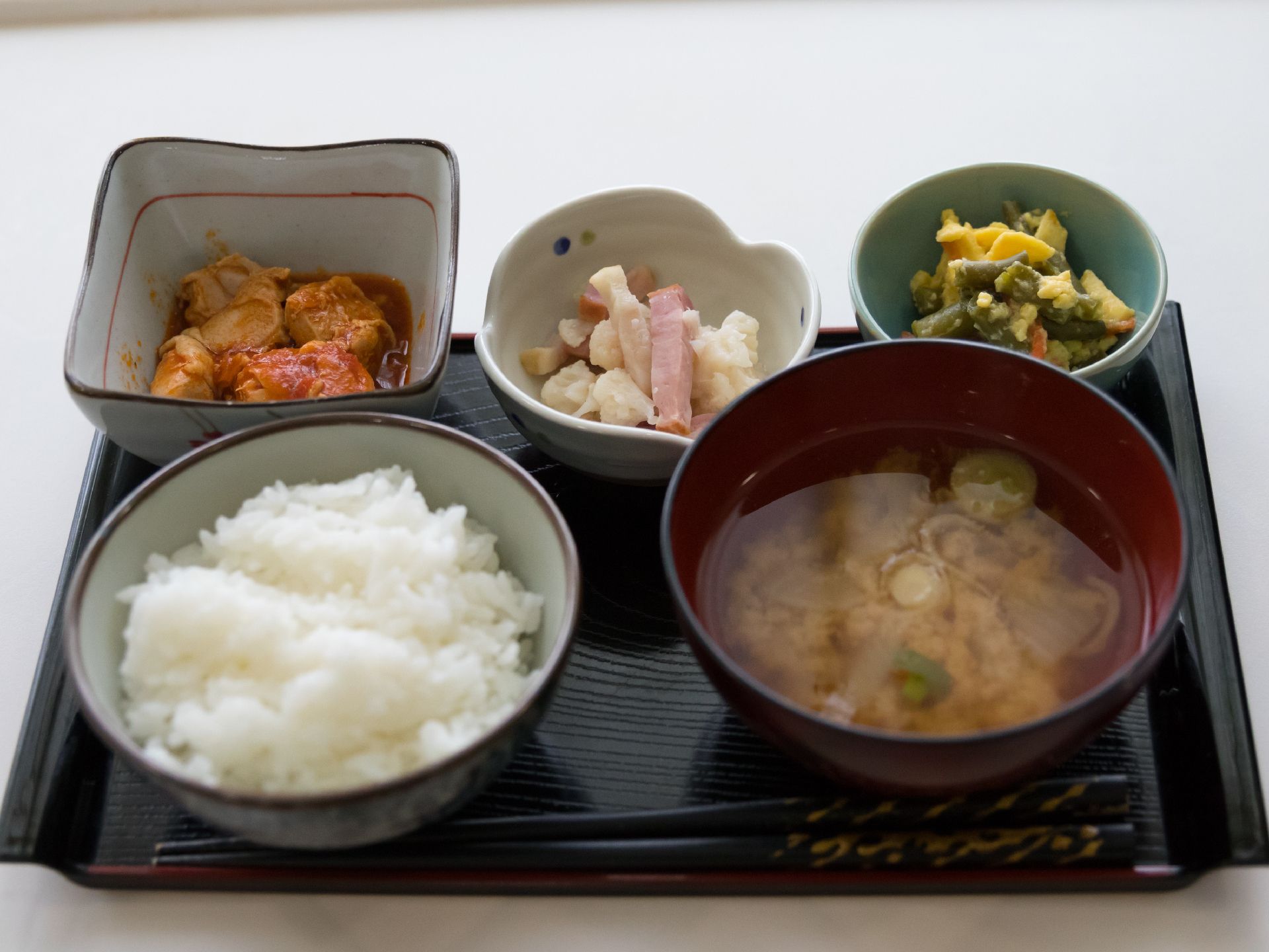 小さめのお盆に、ご飯、みそ汁、小鉢が3つセットされている。ご飯は白米。小鉢は肉、野菜の和え物、サラダになっている。