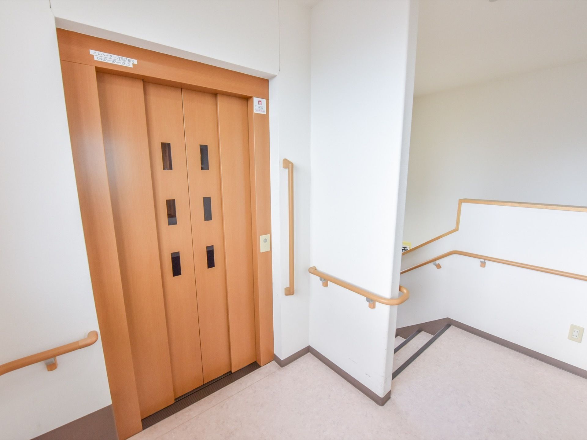 施設内には、扉がライトブラウンのエレベーターが設置されている。右側に階段がある。手すりが柱や壁に取り付けられている。
