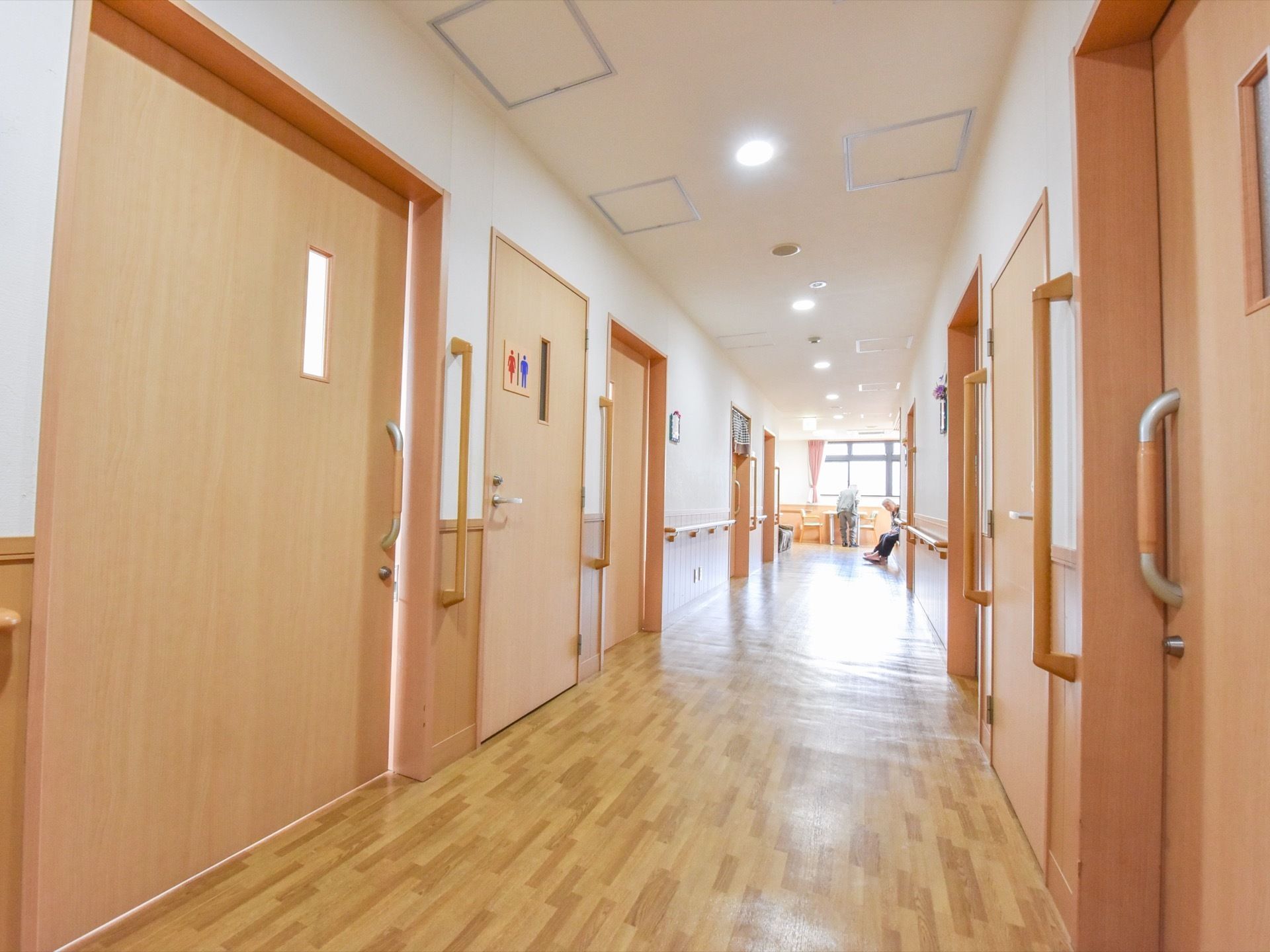 幅が広く明るい廊下である。居室やトイレのドアが両サイドに並んでいる。壁や柱には、手すりが設置されている。