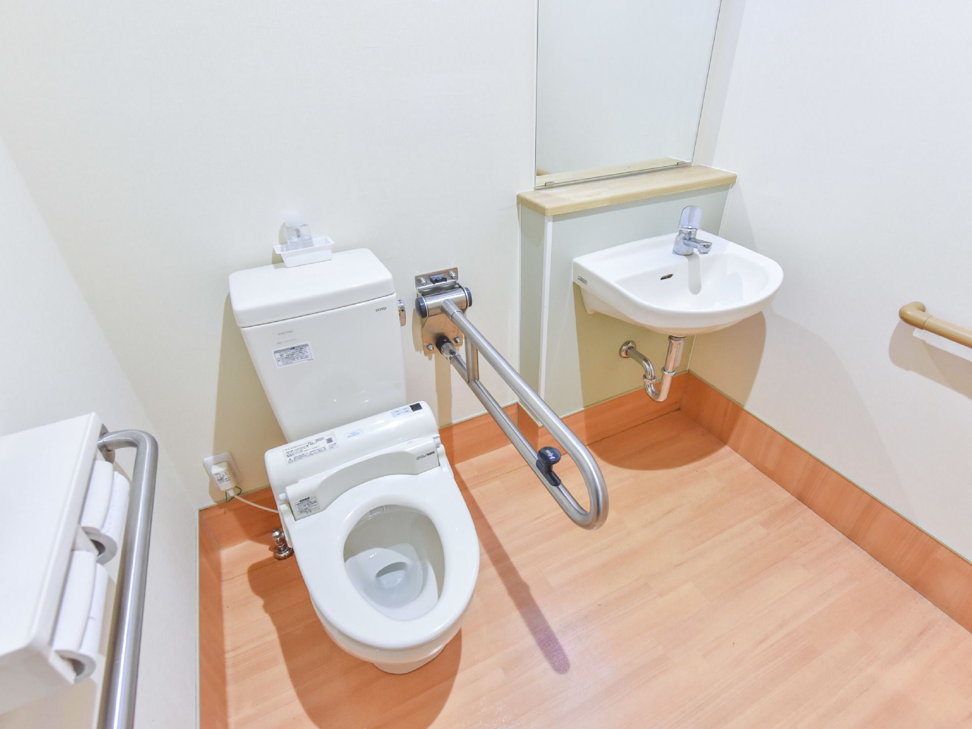 左手にトイレがついており右手に可動式の手すりが設置されている。右側には大きな鏡があり手前に手洗い場がある。