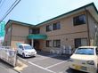 2階建のL字型の建物になっており中央に雨よけのついた入り口がある。目の前は駐車場になっており白いフェンスがついている。