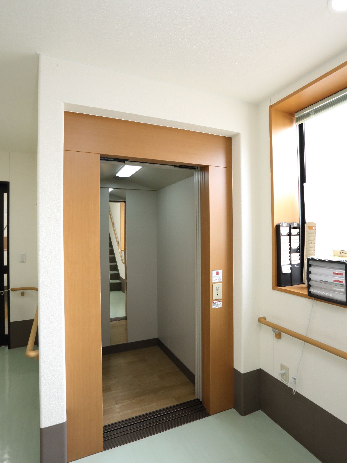 上下階の移動に利用できるエレベーターが施設内に完備されている。照明や鏡が内部に設置されている。扉横の壁には、窓や手すりがある。