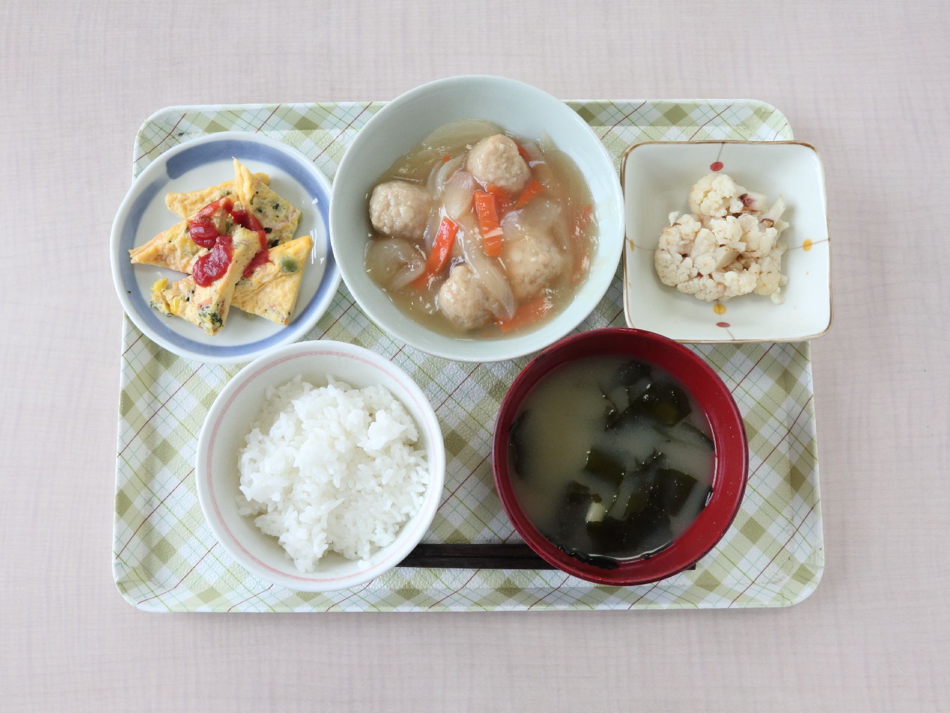 チェックのトレーでお一人おひとりに食事を提供している。ご飯やみそ汁、野菜や卵、肉を使ったおかずが並べられている。
