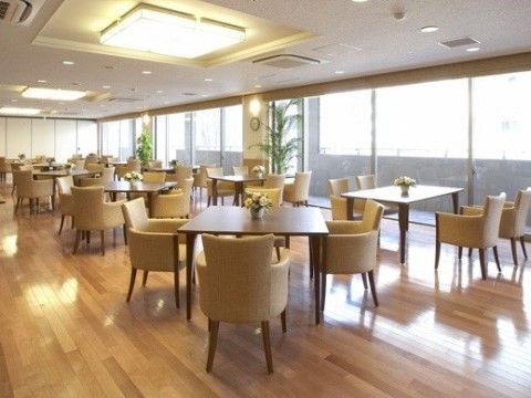 フローリングを採用した広い空間に、穏やかな色調の椅子やテーブルが置かれている。テーブルの上には花が飾られている。