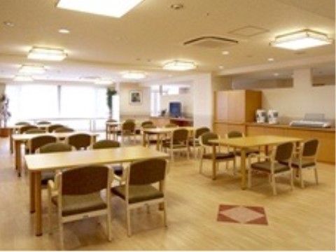 共有スペースは、奥の窓から自然光が入って明るい。茶系でコーディネートされた空間に、4人掛けのテーブルが広い間隔で並べられている。