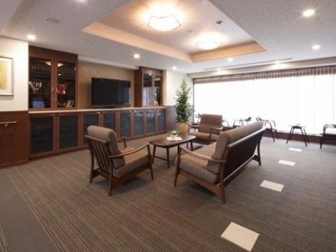 壁面には扉のついた腰高の家具と背の高い家具があり、その中央には大型テレビが置かれている。部屋の隅には鉢植えのグリーンがある。